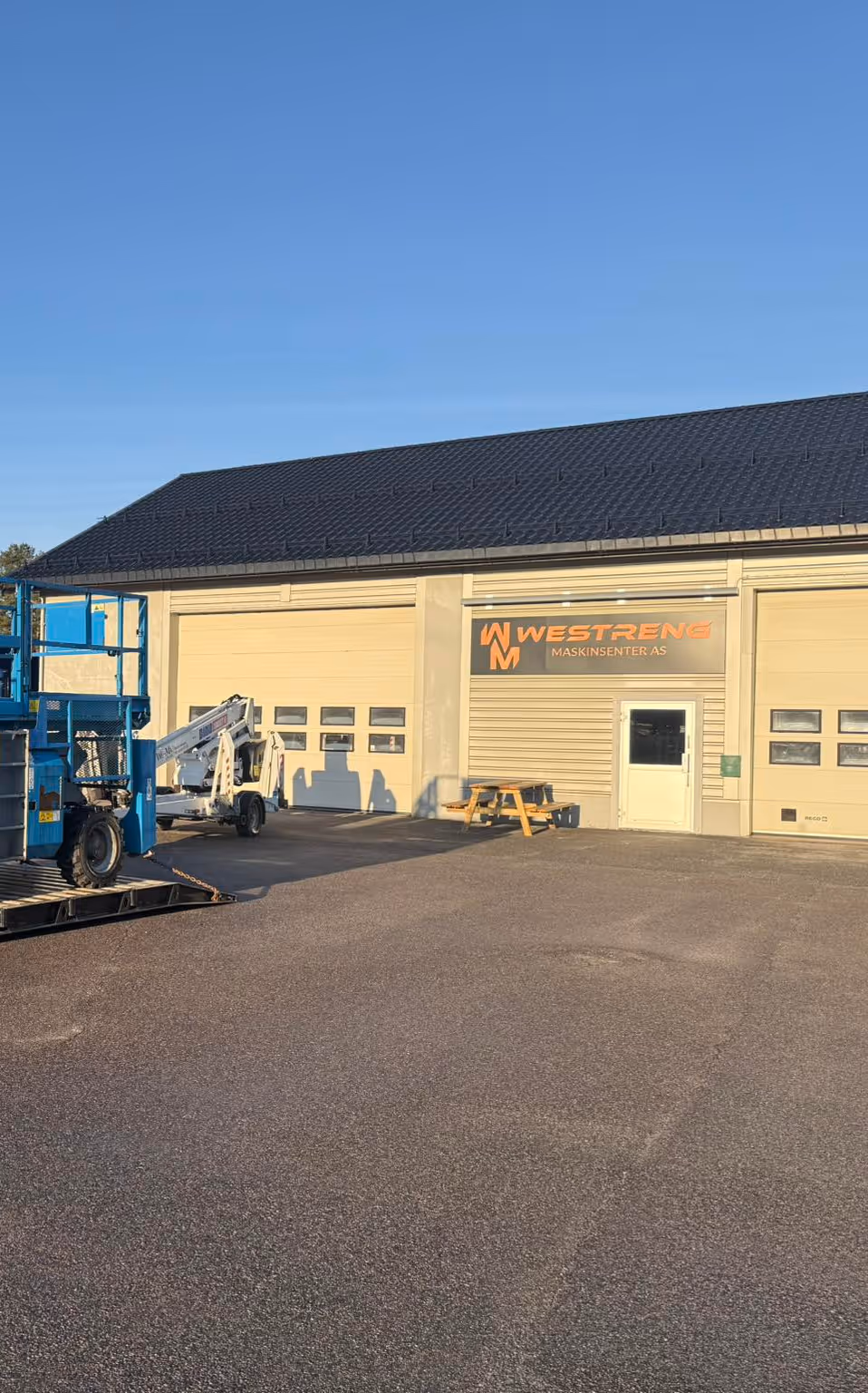 Commercial building with a sign reading 'WESTRENG MASKINSENTER AS' and equipment parked outside on an asphalt lot.